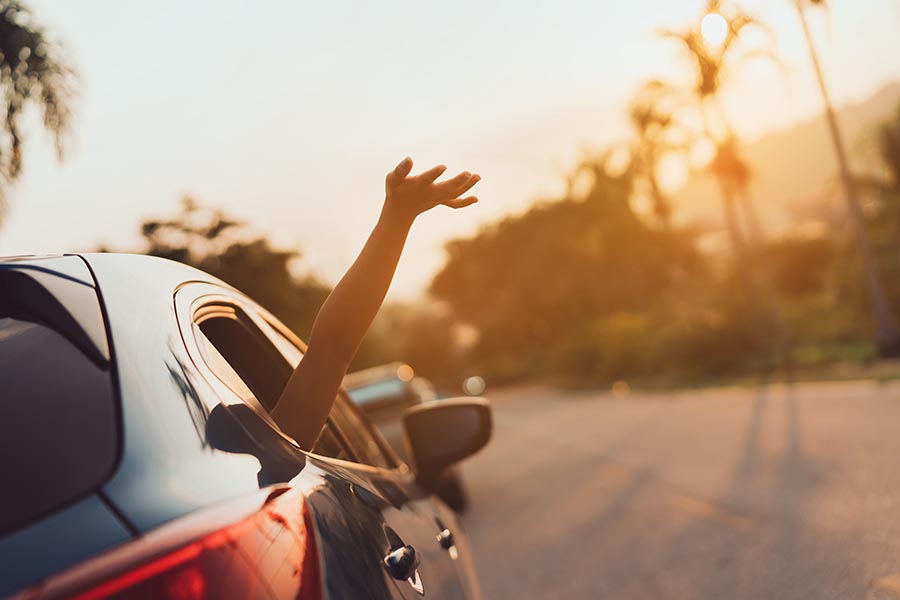 About Our Agency - Hand Waving on the Window of a Car Driving Along a Winding Road at Sunset